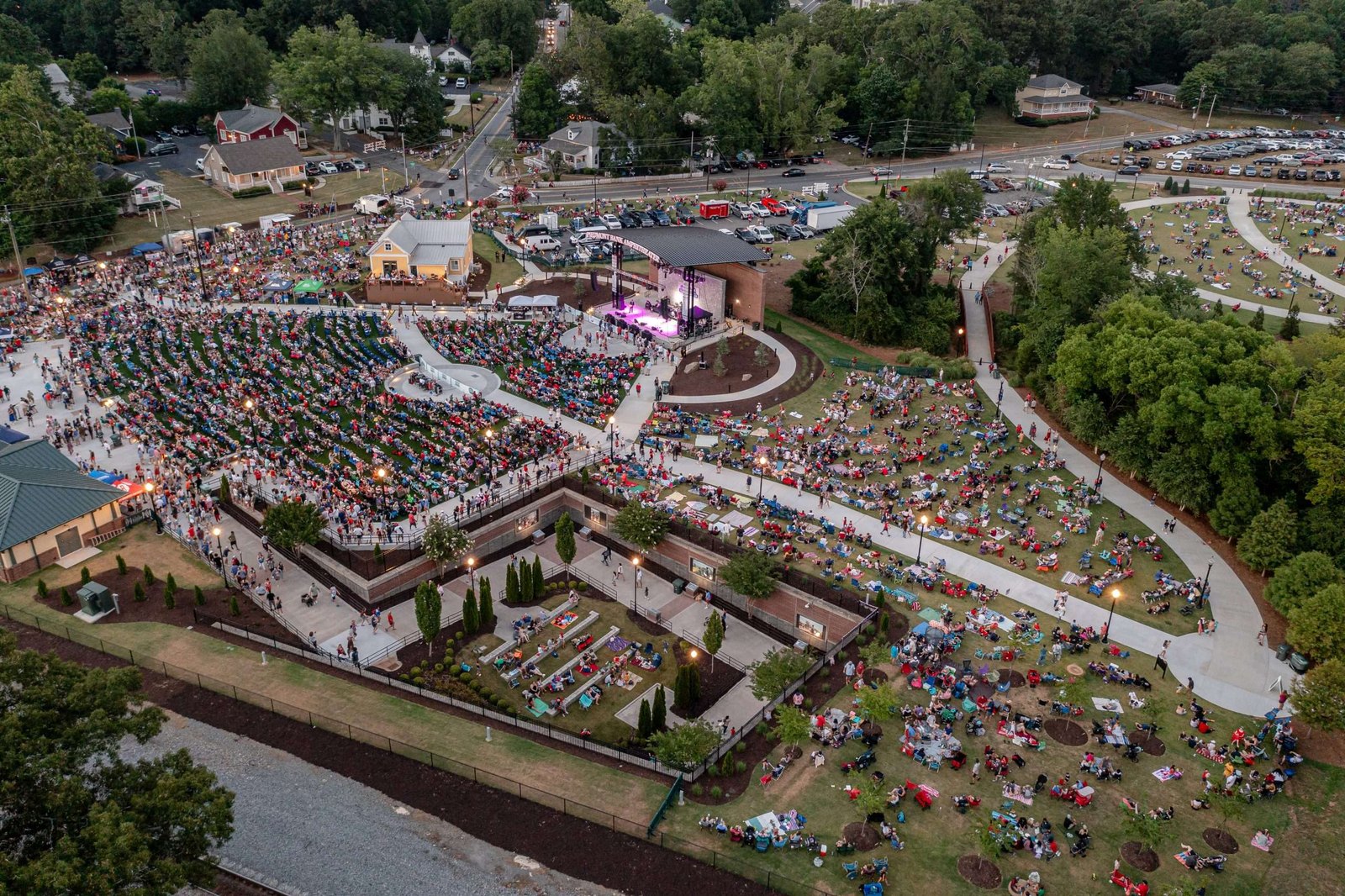 Aerial view of thousands of people filling the amphitheater lawn at Depot Park in downtown Kennesaw at dusk.