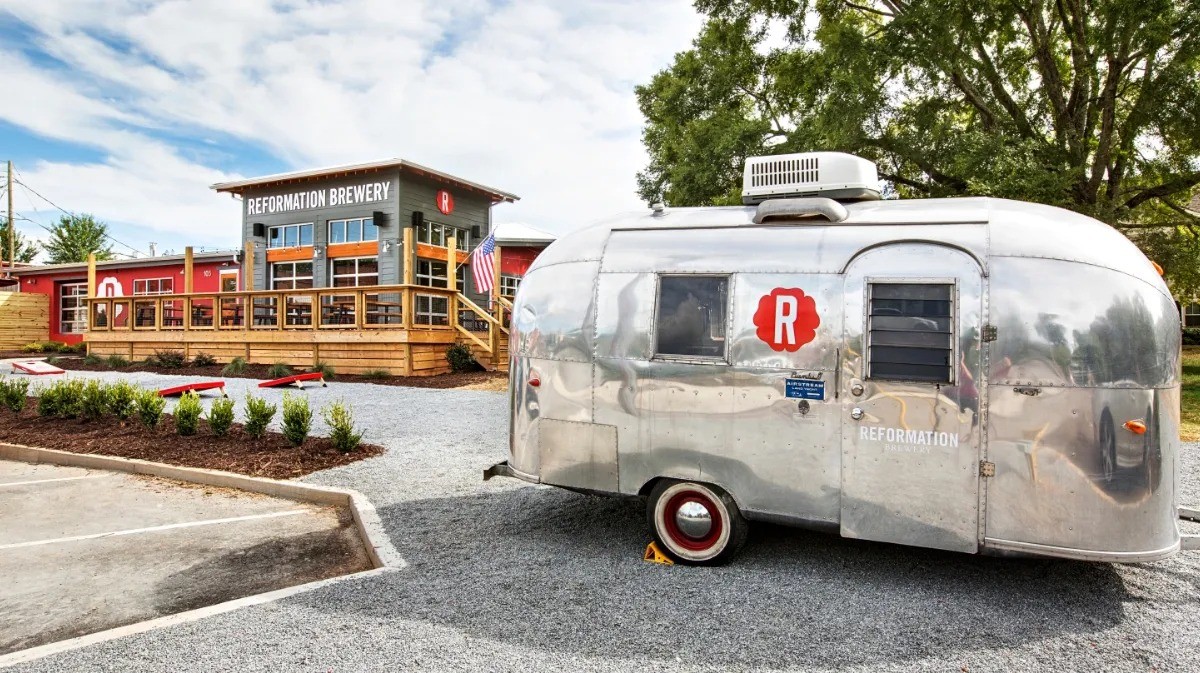 Reformation Brewery's Woodstock taproom: a red and grey building with a large wooden deck, beer garden and a polished Airstream trailer in the gravel lot.